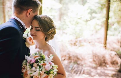 a bride and groom standing in the woods.